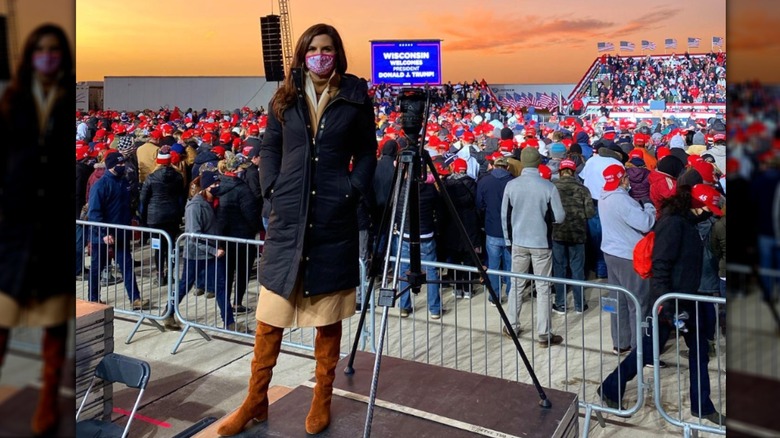 Kaitlan Collins stands at a Trump campaign rally wearing a blue puffer coat