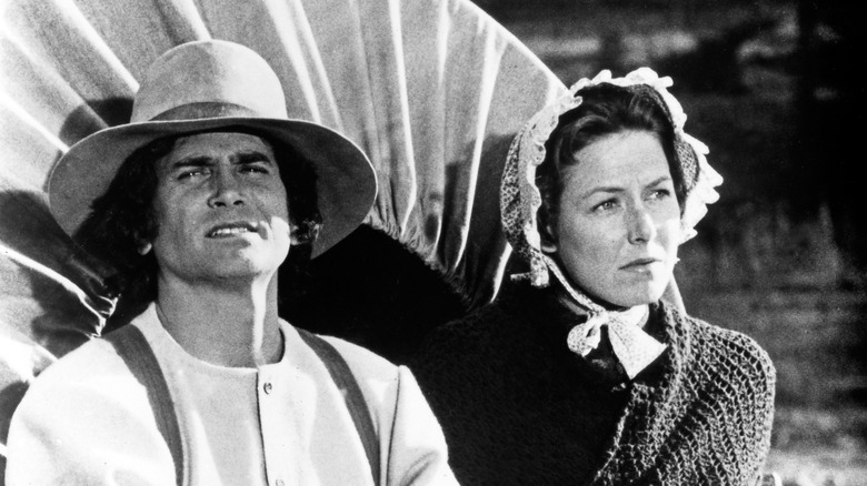 Little House on the Prairie characters Ma and Pa sit on a covered wagon, looking into the distance