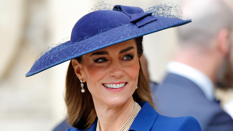 Kate Middleton smiles wearing a blue jacket and a blue fascinator