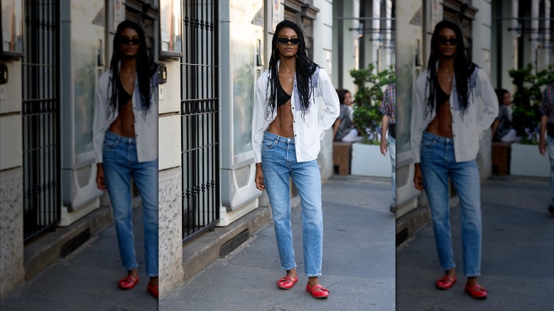 A woman in a white button down, jeans, and red ballet flats.