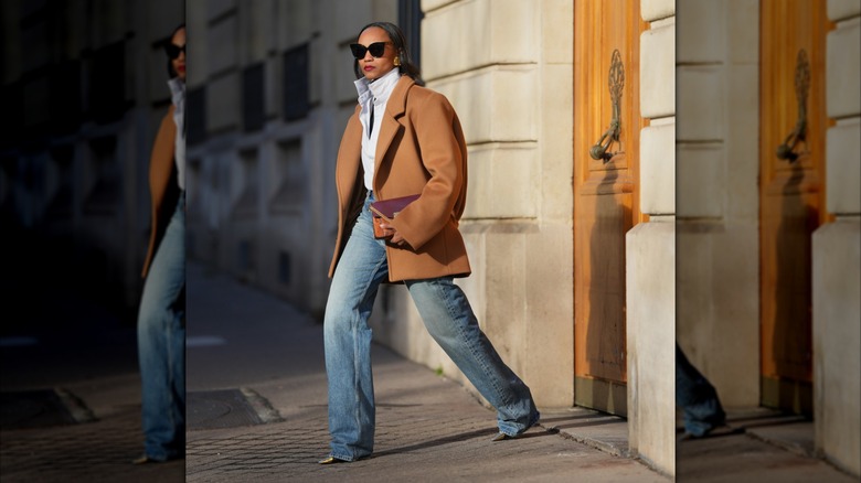 A woman in a white button down, jeans, and a brown coat.