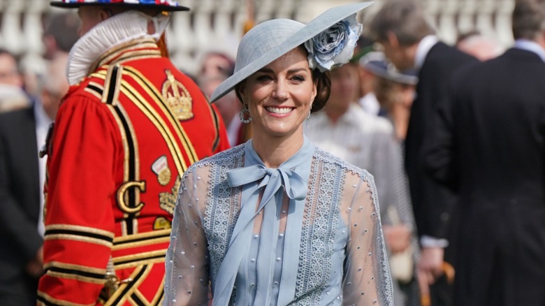 Kate Middleton wearing a blue dress with sheer sleeves and a blue wide-brimmed hat at King Charles' Coronation Garden Party.