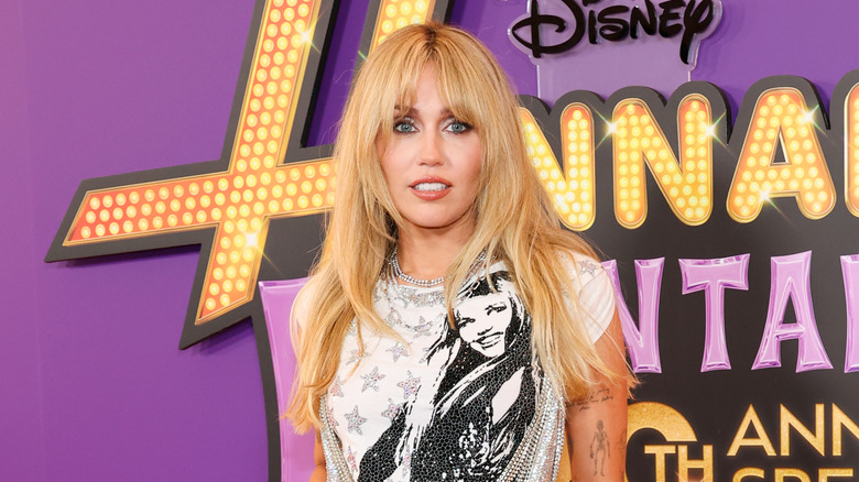 Miley Cyrus poses wearing an embellished white T-shirt and a crystal necklace