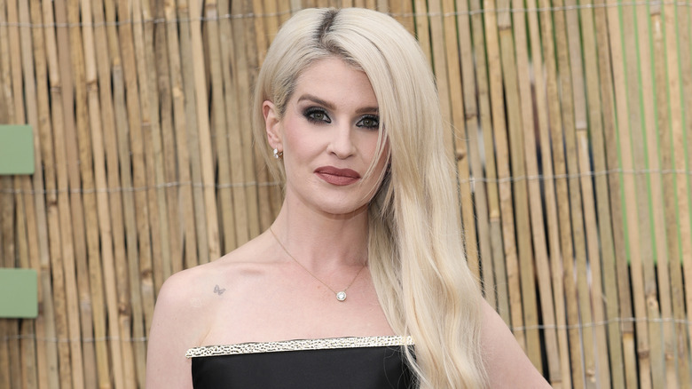 Kelly Osbourne with blond hair posing in a black strapless dress