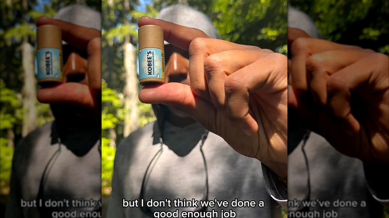 Kobe Harris in a gray hoodie holding up on of his brand's lip balms.