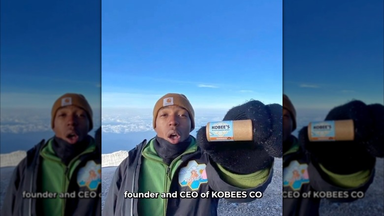 Kobe Harris in the snowy mountains holding up a Kobee Lip balm