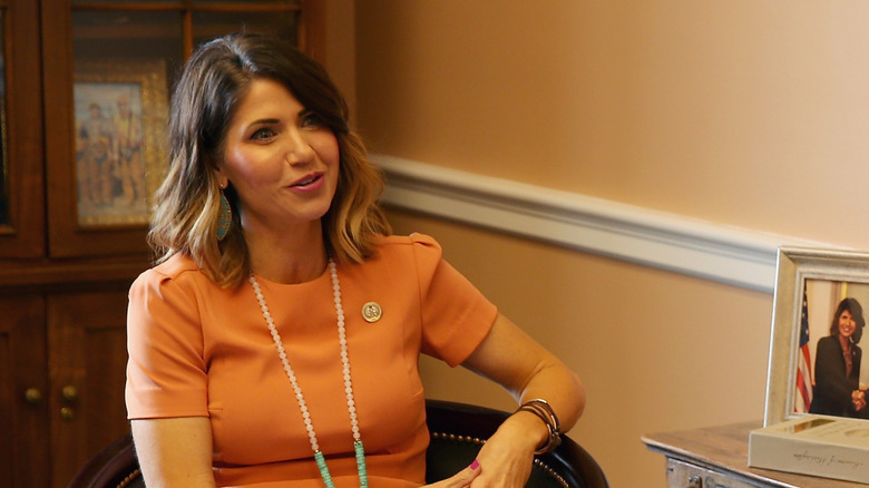 Kristi Noem talking while wearing an orange dress