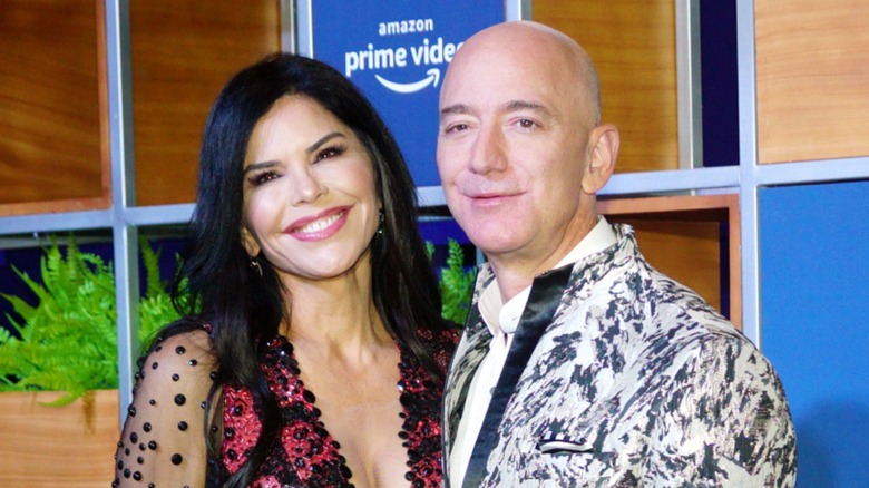 Cropped image of Lauren Sánchez Bezos and Jeff Bezos. They are standing in front of an Amazon Prime Video backdrop. Lauren is a woman with pale skin and dark hair. Jeff is a man with fair skin and a bald head.