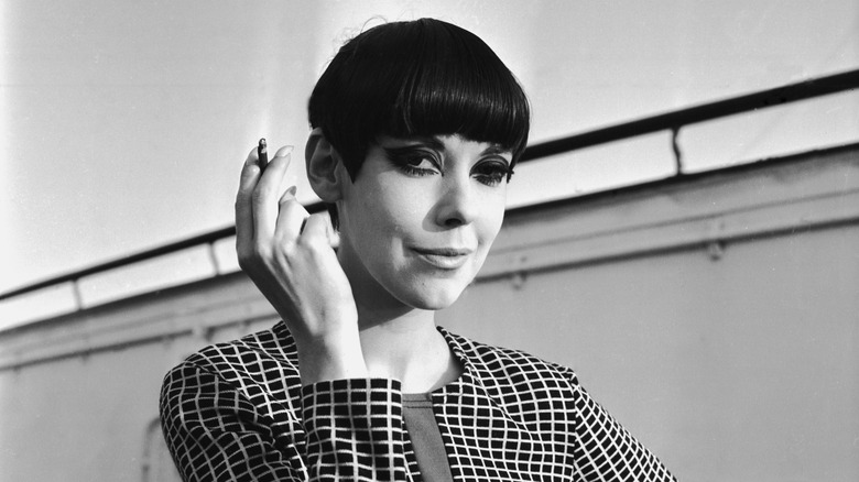 Peggy Moffitt smoking a cigarette wearing a checkered jacket.