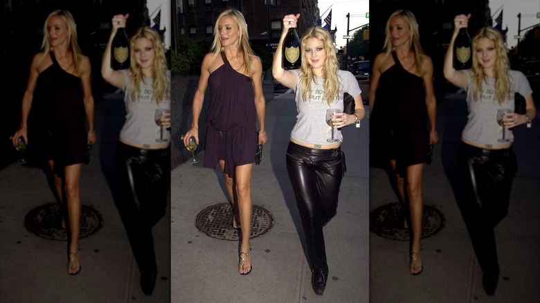 Drew Barrymore holding a bottle and glass of champagne wearing leather pants and a tee walking with Cameron Diaz  wearing a messy purple dress.