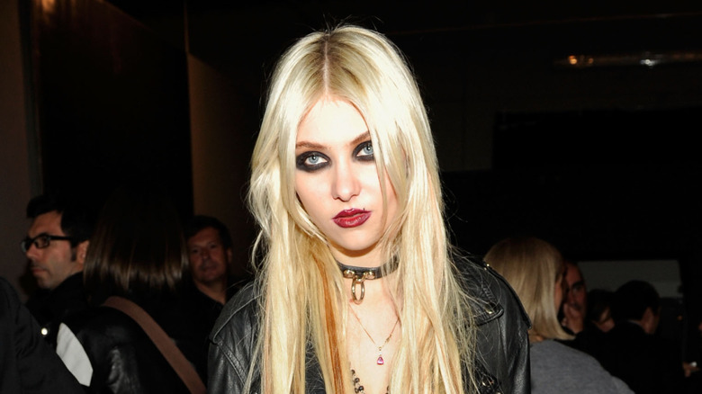 Taylor Momsen wearing dark smudged eye makeup and a red lip with a punk choker necklace and black leather jacket.