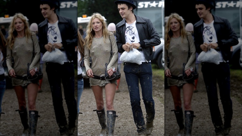 Kate Moss wearing a disheveled outfit with tall boots and Pete Doherty wearing jeans, a white shirt, and black bomber jacket, walking outside.