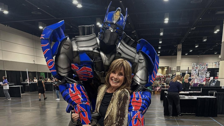 Linda Gray poses with someone dressed in a Transformers costume in an event hall