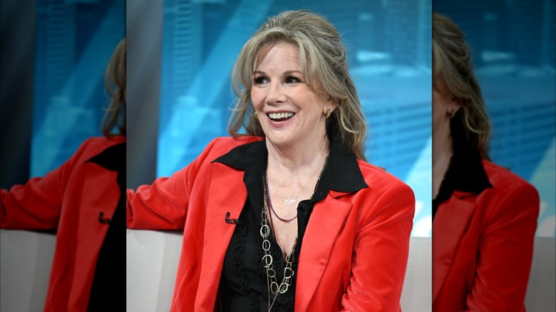 Melissa Gilbert smiles wearing a voluminous hairstyle and a red blazer