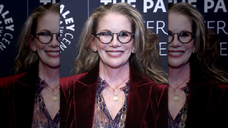 Melissa Gilbert smiles wearing round glasses and a red velvet blazer