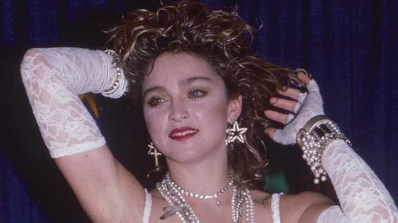 Madonna with her hands by her head wearing white lace gloves and lots of statement jewelry at the MTV Video Music Awards.