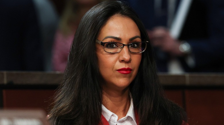 Lauren Boebert at a hearing. She is a woman with dark hair and a spray tan. She is wearing dark-framed glasses and red lipstick.