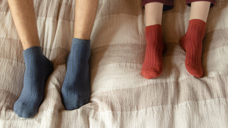 two feet wearing socks in bed blue and red socks