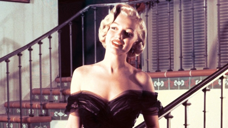 Marilyn Monroe standing on a staircase wearing a black off-the-shoulder tulle gown in 1950, the same dress she wore to the 23rd annual Academy Awards in 1951