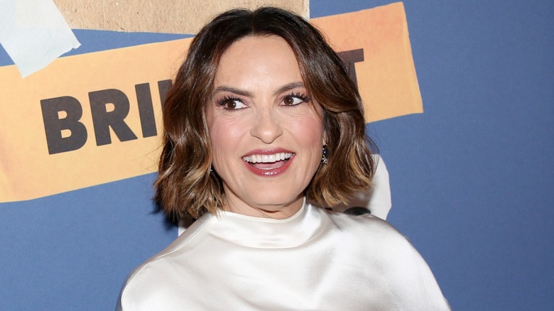 Mariska Hargitay smiling at a red carpet event wearing a silky high-neck top with glossy lips and a wavy bob.
