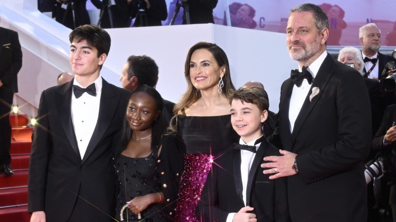 Mariska Hargitay posing on a red carpet wearing a red sparkly dress standing next to her kids and husband.