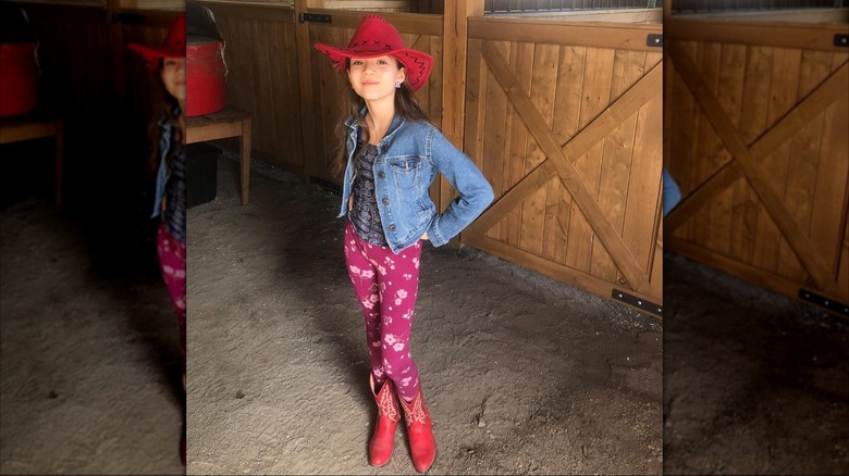 Skywalker Hughes smiling in a red cowgirl hat and boots with prink floral-print leggings and a denim jacket.