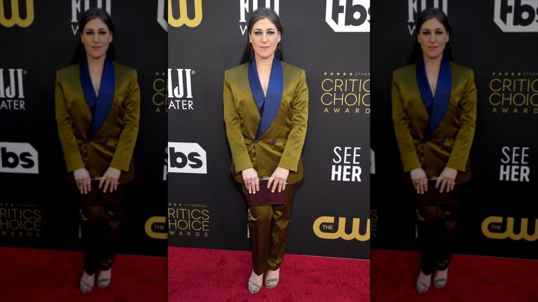 Mayim Bialik smiles wearing a gold-and-blue suit on the red carpet.