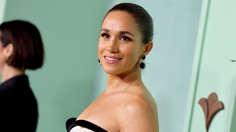 Megan Markle smiling with her hair in a slicked bun and ivory and black dress.
