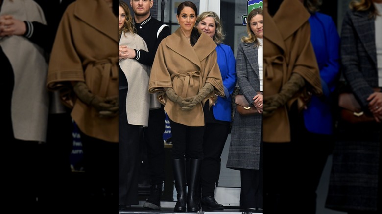 Meghan Markle wearing light brown cloak with black tailored pants and tall leather riding boots at Invictus One Year to Go event.