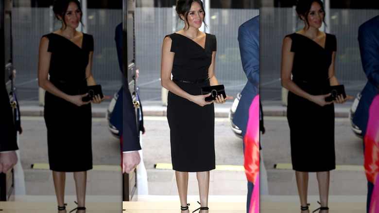 Meghan Markle wears an elegant black midi dress and carries a clutch purse