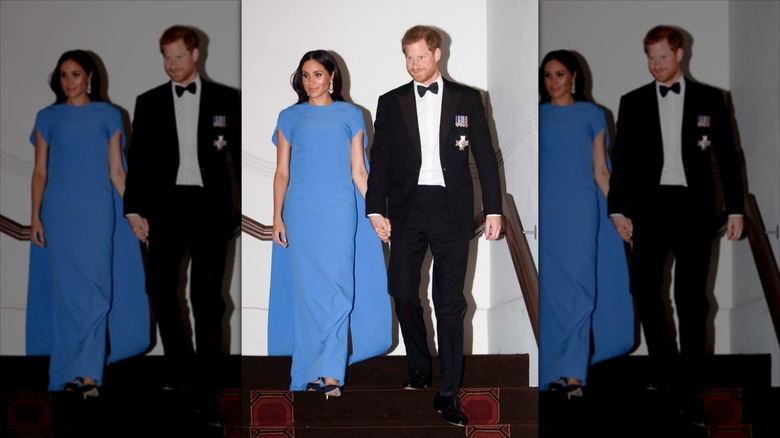 Meghan Markle wearing a blue cape dress next to Prince Harry wearing a tuxedo