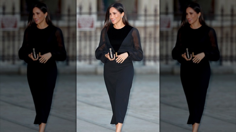 Meghan Markle walks wearing a black dress with sheer balloon sleeves