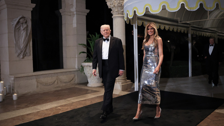 Melania Trump wearing a silver dress and walking with Donald Trump