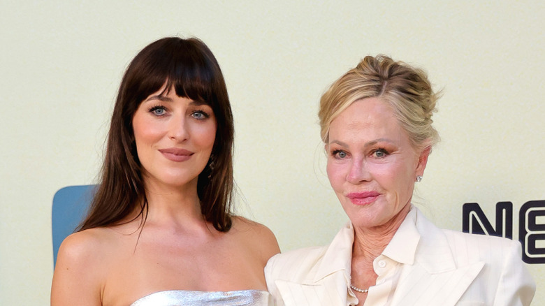 Dakota Johnson and Melanie Griffith pose together smiling on a red carpet at a premiere