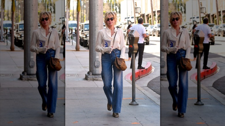 Melanie Griffith holds a book wearing wide-leg jeans and a white blouse