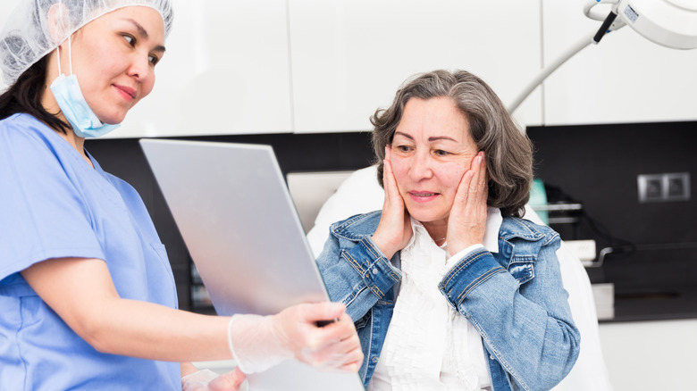 An older woman sitting in a medical practioners office looking in the mirror the medical practitioner is offering her