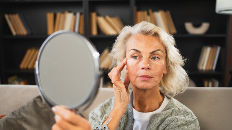 An older woman looking in the mirror and touching her face with one hand