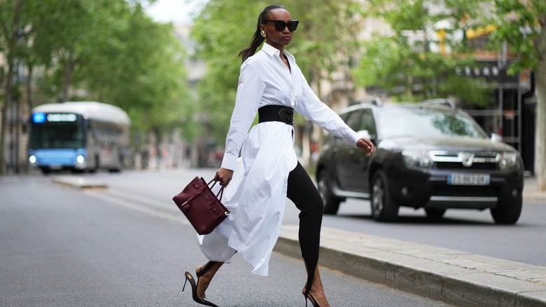 A woman walks down the street in a long white button-up dress layered over black skinny jeans.
