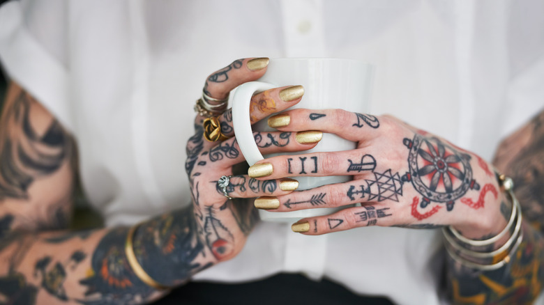 A person with tattooed hands and knuckles holding a mug