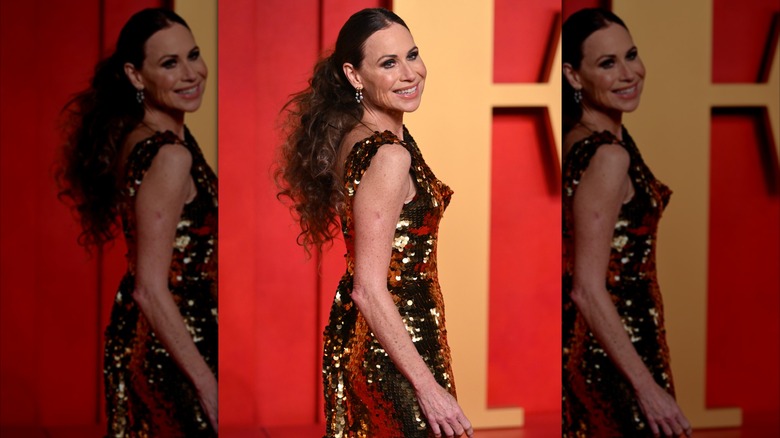 Minnie Driver wearing a sparkling gold dress with her hair in a slicked-back and teased ponytail.