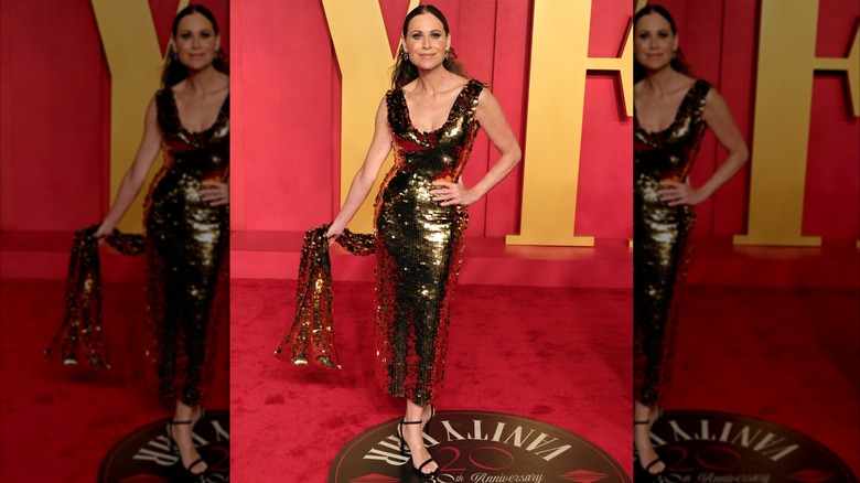 Minnie Driver posing at an Oscars party wearing a shimmering gold dress.