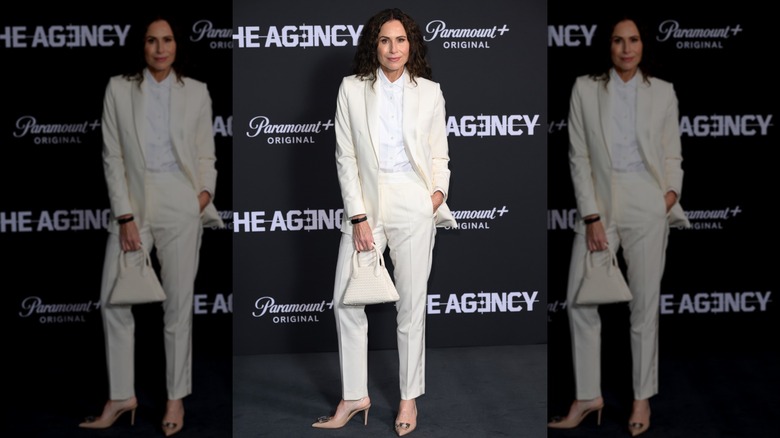 Minnie Driver posing at an event wearing an all-white suit.