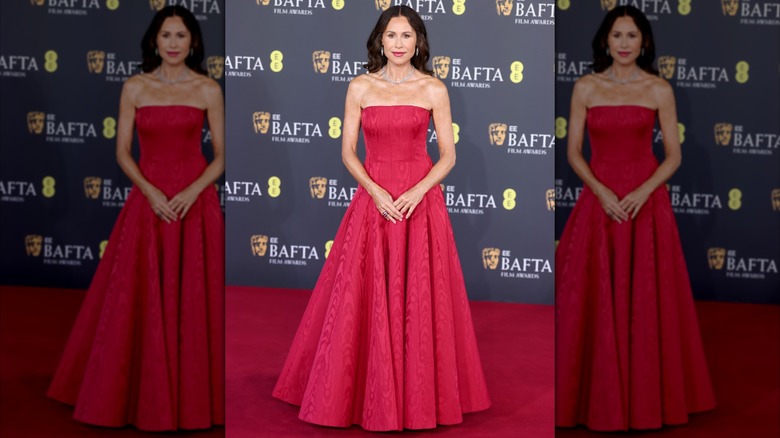 Minnie Driver posing on the red carpet wearing a red strapless ballgown dress.