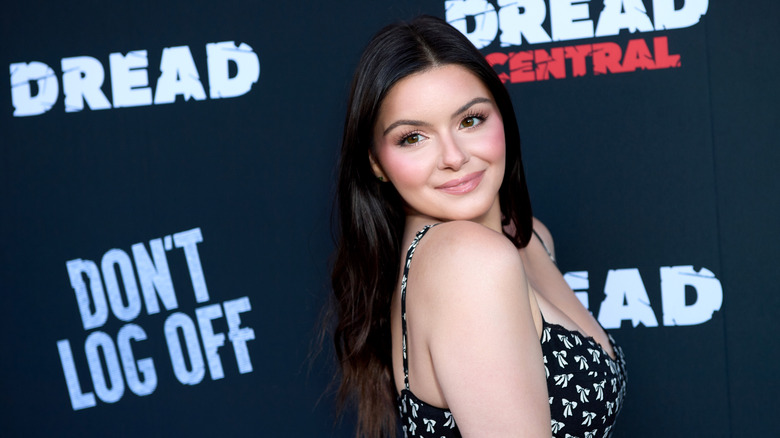 Ariel Winter posing at a red carpet event wearing a black and white dress with her dark, straight hair down.