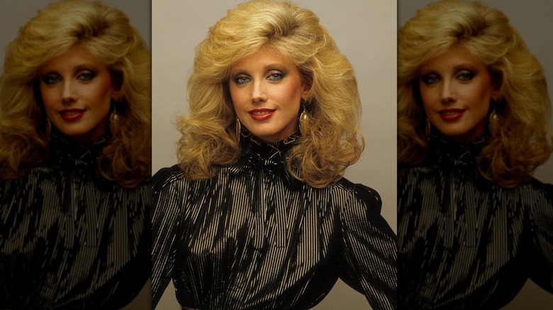 Morgan Fairchild posing in a black top with gold earrings.