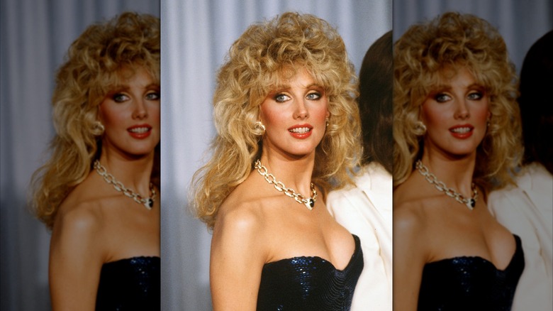 Morgan Fairchild posing in a sparkly blue dress with a gold chain necklace.