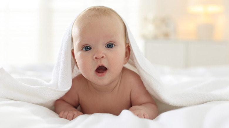 Baby with mouth open under a towel looking surprised.