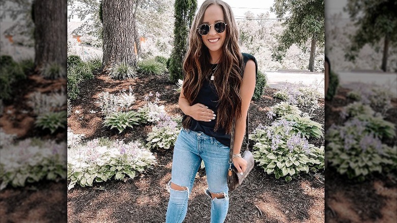 Woman in muscle tank stands near trees