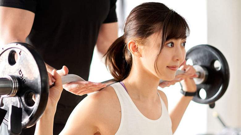 Asian women lifting barbell with spotter