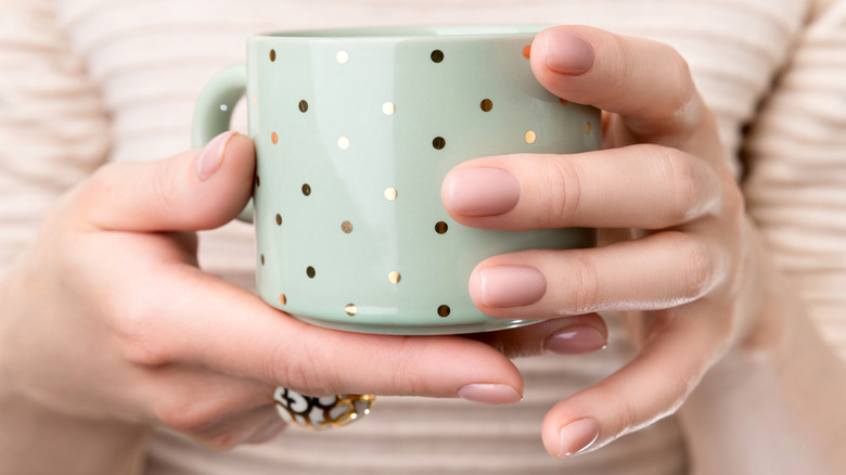 Woman's hands with nude nail polish holding mug